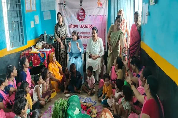 आंगनवाड़ी केंद्र के कमरे में महिलाओं और बच्चों के बीच पोषण सामग्री के साथ आयोजित सामुदायिक कार्यक्रम