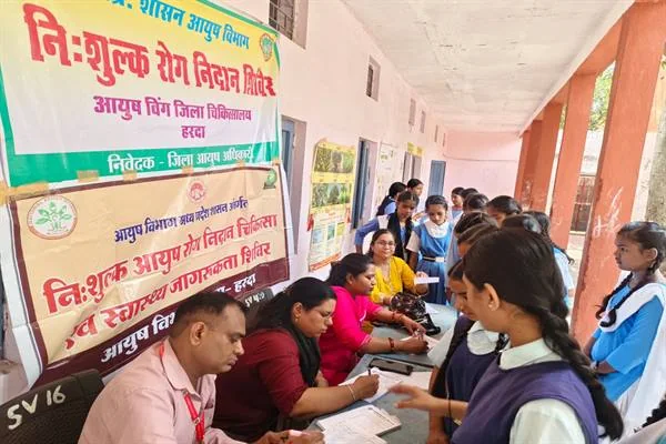 शासकीय कन्या शाला के बरामदे में मेज पर बैठे स्वास्थ्यकर्मी छात्राओं का पंजीयन और जांच करते हुए